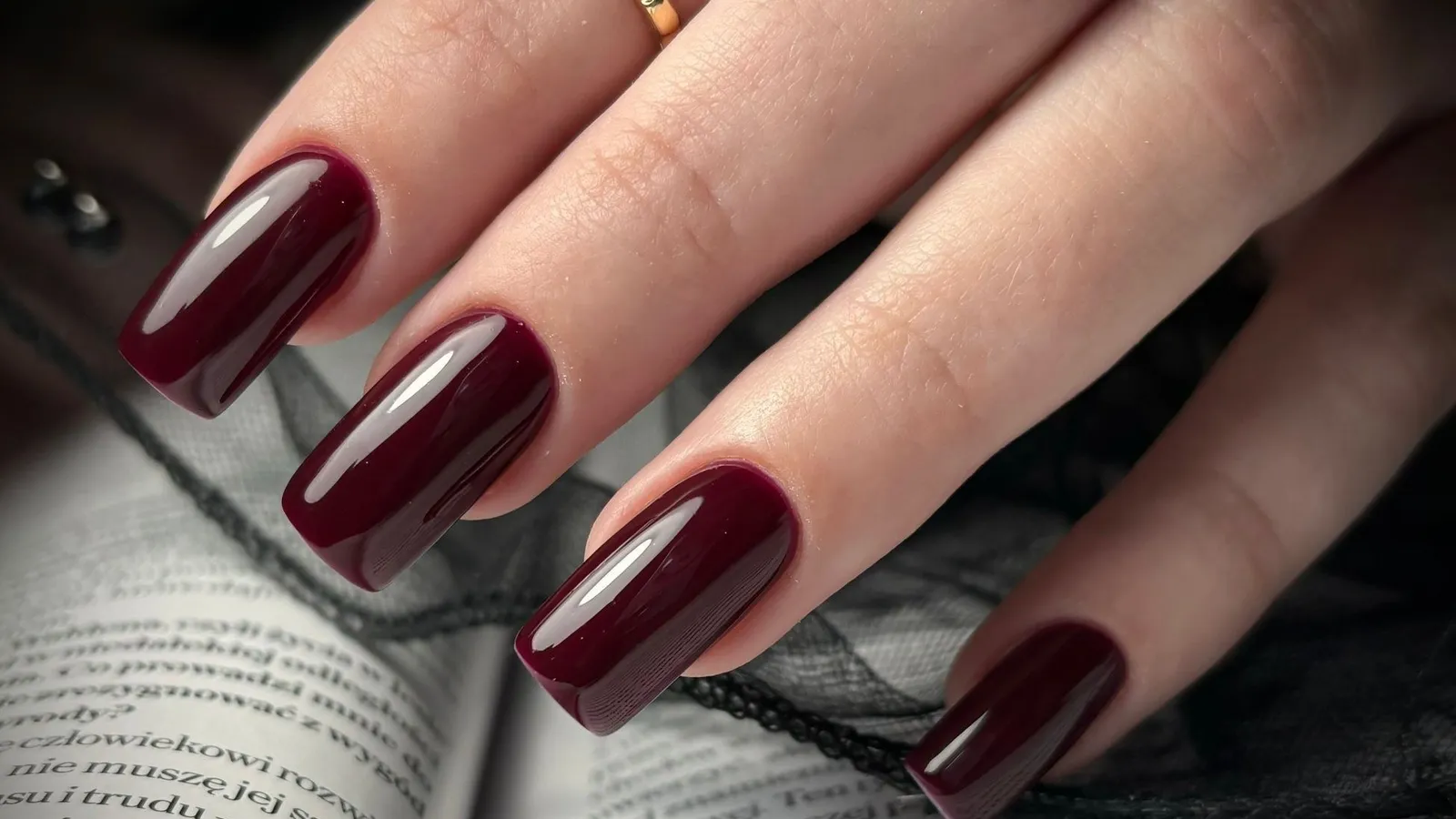 Bordowy manicure z naszego salonu na tle książki
